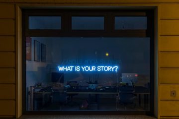 window with a neon sign reading, "What is your story?"