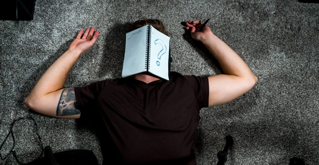 Person laying on the ground with a notebook over their face. They are wondering how to beat writer's block.